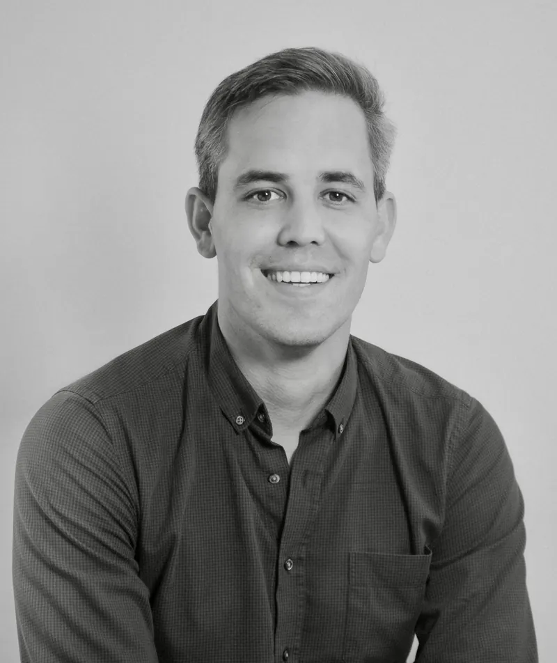 Portrait corporate en noir et blanc d’un homme souriant en chemise sombre sur fond clair