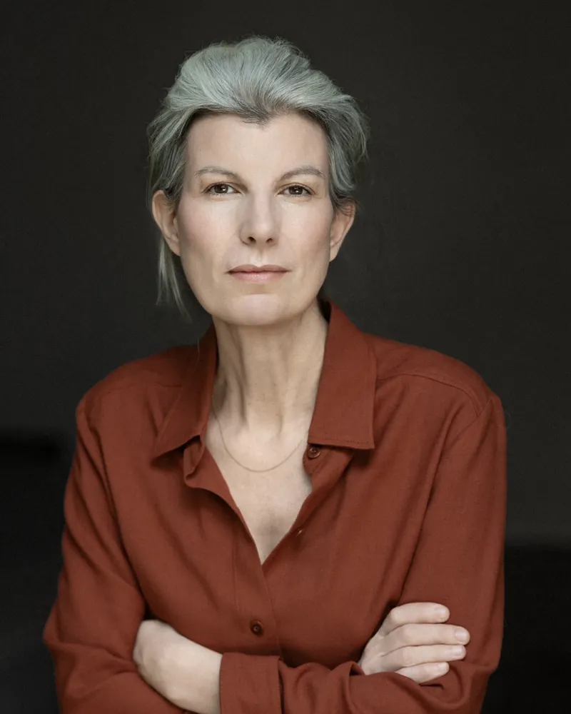 Portrait corporate d'une femme aux cheveux gris en chemise terracotta, bras croisés